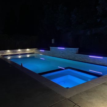 A modern swimming pool at night in San Jose, illuminated by soft blue and purple lights, serviced by Olivera Pool Services.
